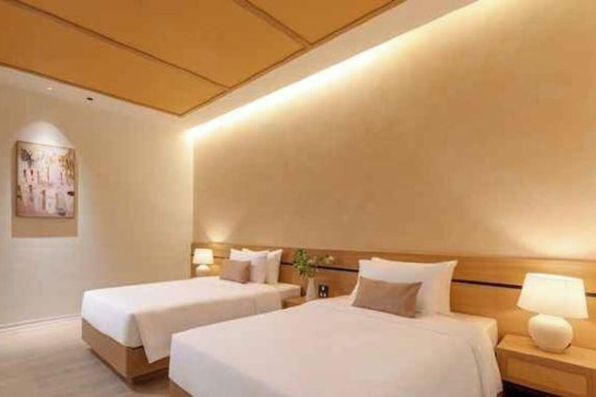 Una habitación de hotel con dos camas, una mesita de noche con lámpara y una obra de arte colgada en la pared.