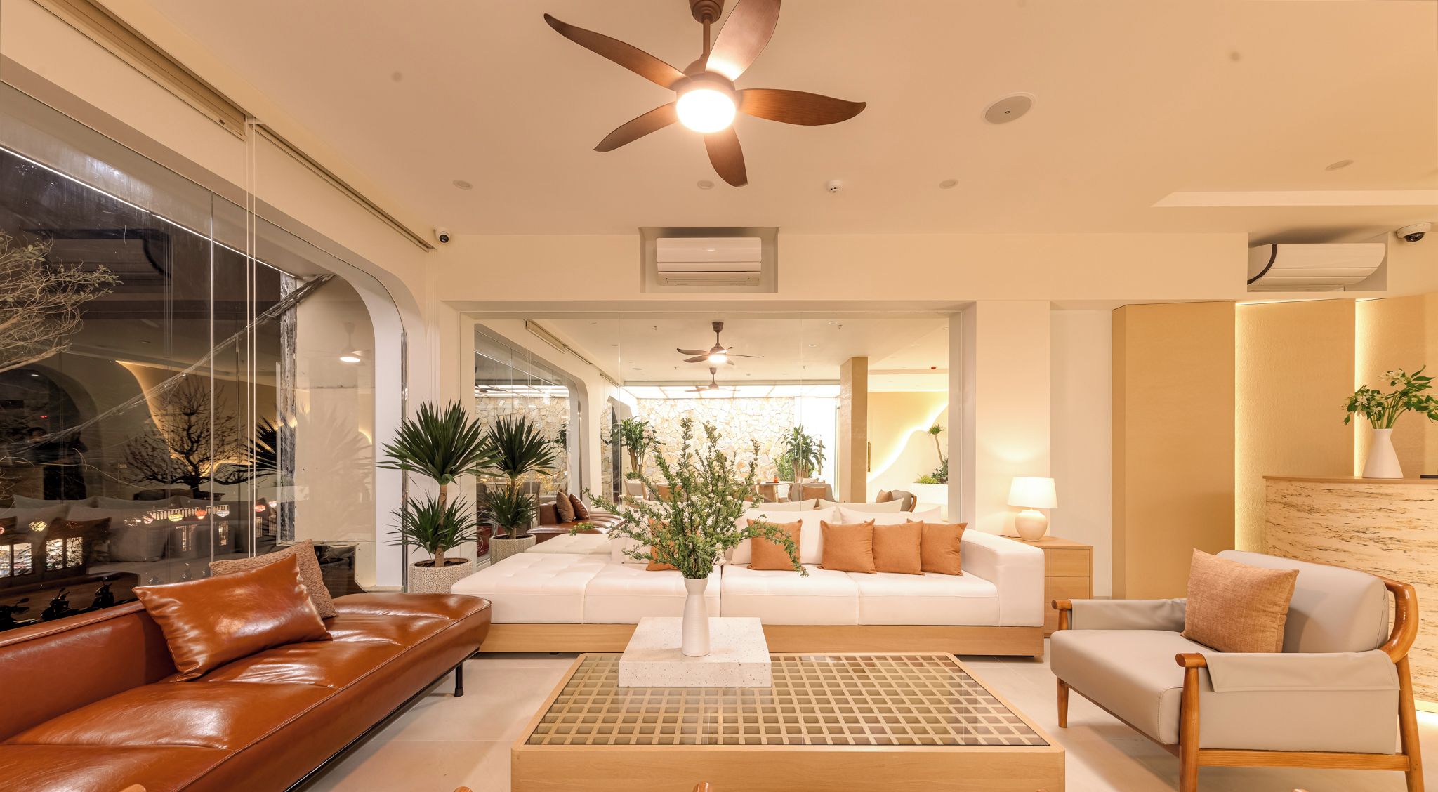 A modern hotel lobby with leather sofas, a wooden coffee table, and a large plant centerpiece.