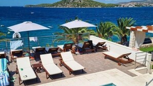 A poolside area with lounge chairs and umbrellas, overlooking a body of water and a distant island.