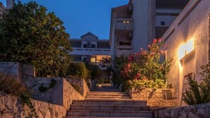 A stone staircase leading to a building with a balcony, surrounded by greenery and flowering plants.