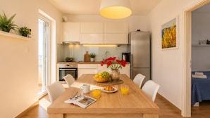 Una cocina moderna con armarios blancos, un refrigerador de acero inoxidable y una zona de comedor con mesa de madera.
