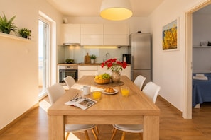 Una cocina moderna con armarios blancos, un refrigerador de acero inoxidable y una zona de comedor con mesa de madera.