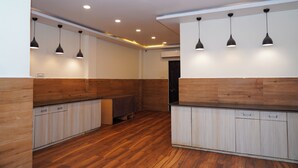 A modern kitchen with wooden cabinets, pendant lights, and a wooden floor. - Hotel Happy Stay  (Bhopal)