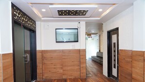 A hallway with wooden paneling, a flat-screen TV mounted on the wall, and a door with a handle. - Hotel Happy Stay  (Bhopal)