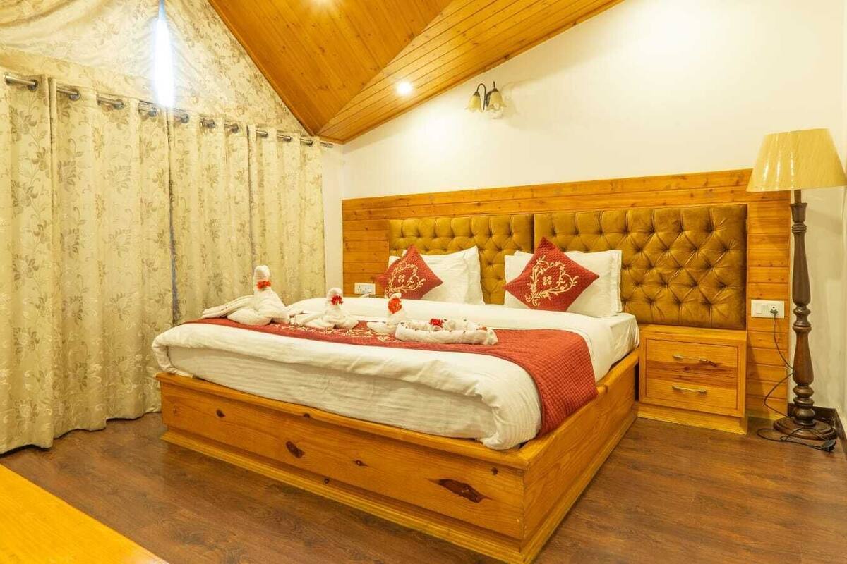 A bedroom with a wooden bed, a nightstand, a lamp, and a window with curtains.