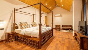 A four-poster bed with a wooden frame and intricate carvings, a wooden nightstand, a wooden bench, and a television on a wooden cabinet. - Smile Resort (Bhuntar)