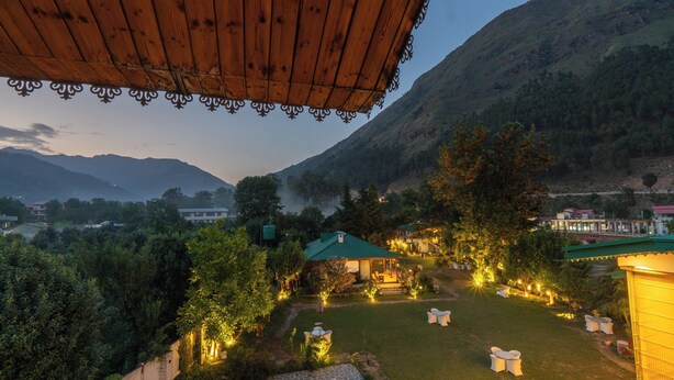 A courtyard with outdoor seating, surrounded by lush greenery and mountains in the background. - Smile Resort (Bhuntar)