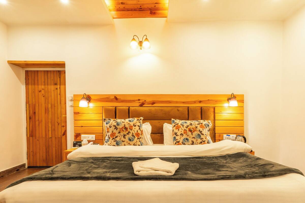 A bedroom with a wooden headboard, two bedside lamps, a bed with white and floral pillows, and a folded towel on the bed.