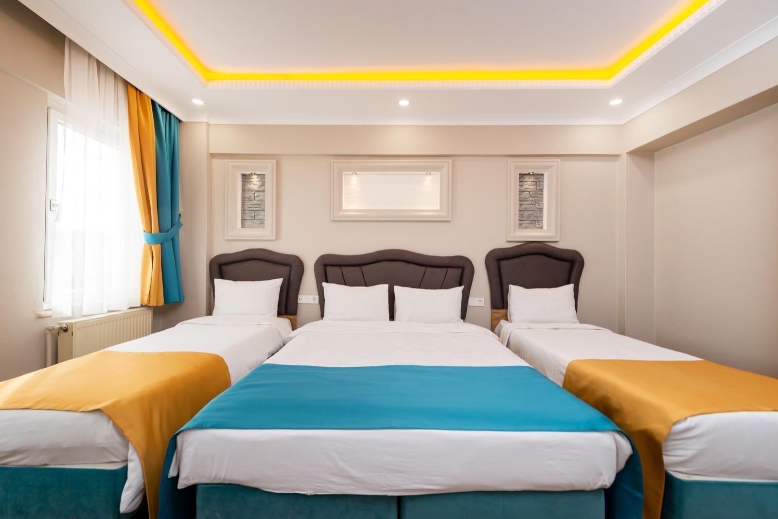 A hotel room with three beds, a large window with curtains, and a ceiling with recessed lighting.