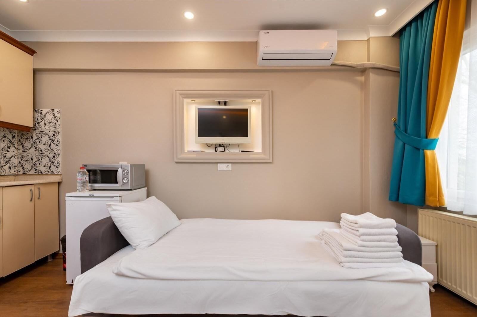 Una habitación de hotel con una cama, televisión montada en la pared, microondas y radiador.