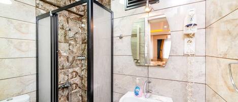 A bathroom with a glass shower enclosure, a sink, a mirror, and a towel rack.