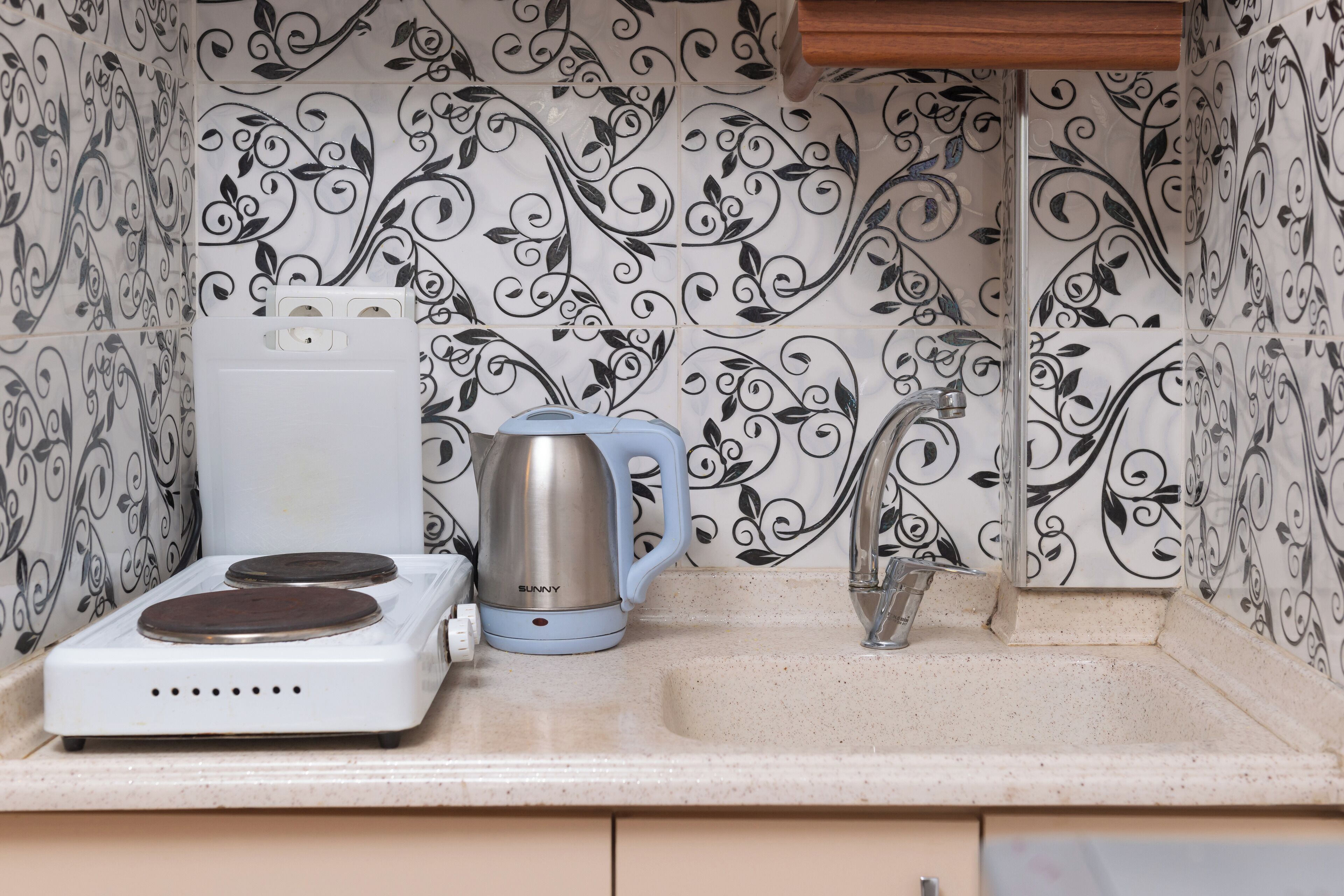 Een keuken met een witte kookplaat, een blauwe elektrische waterkoker en een spoelbak.