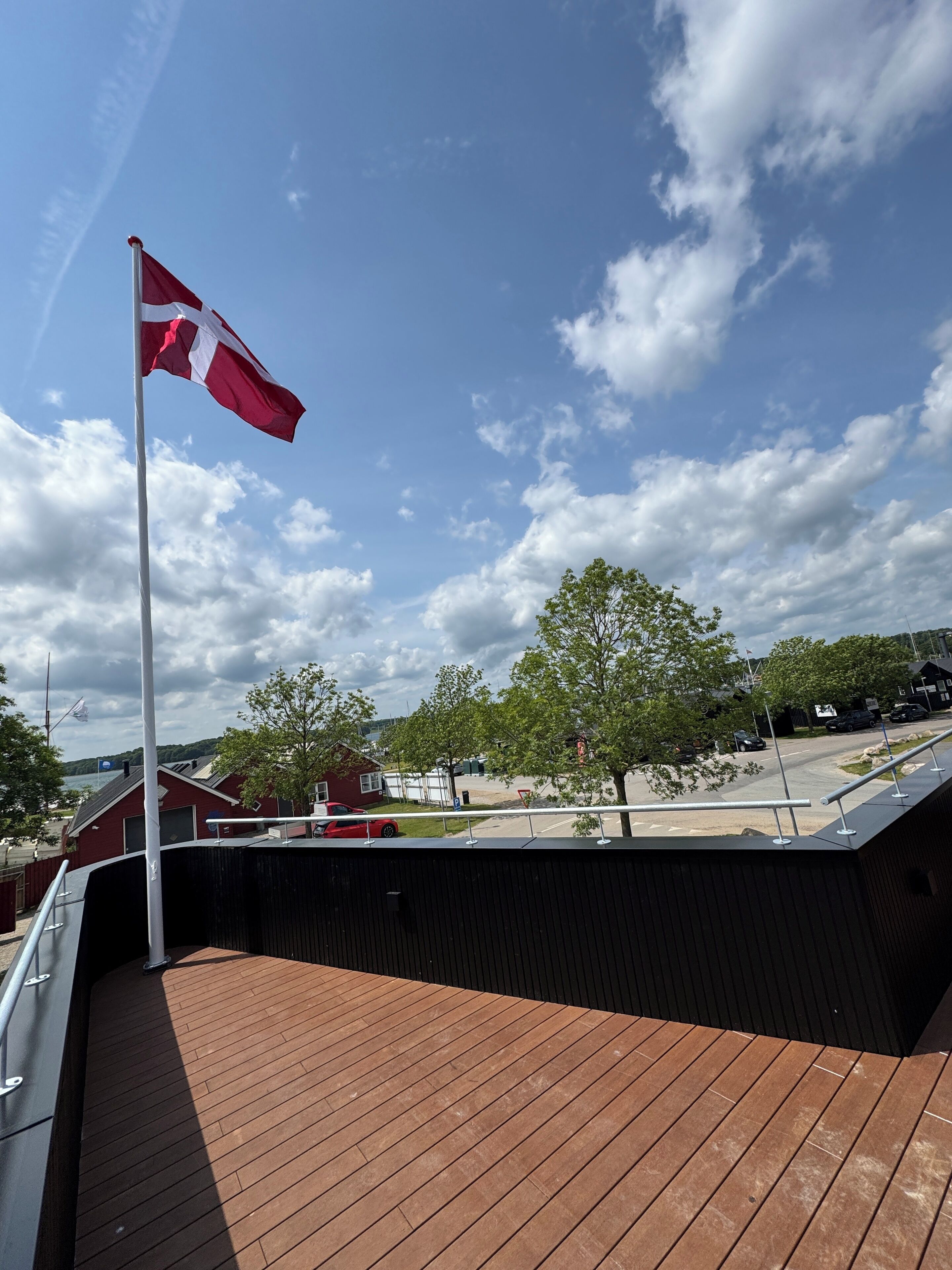 A flag on a flagpole, a wooden deck, and a clear sky with clouds.