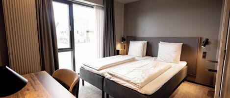 A hotel room with a large bed, a desk, and a window with curtains.