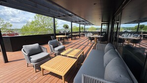 Une terrasse extérieure dotée d’un plancher en bois, de meubles rembourrés de couleur grise et d’une structure en forme de pergola.