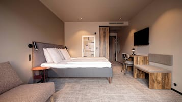 A modern hotel room with a large bed, a desk, a chair, and a TV mounted on the wall.