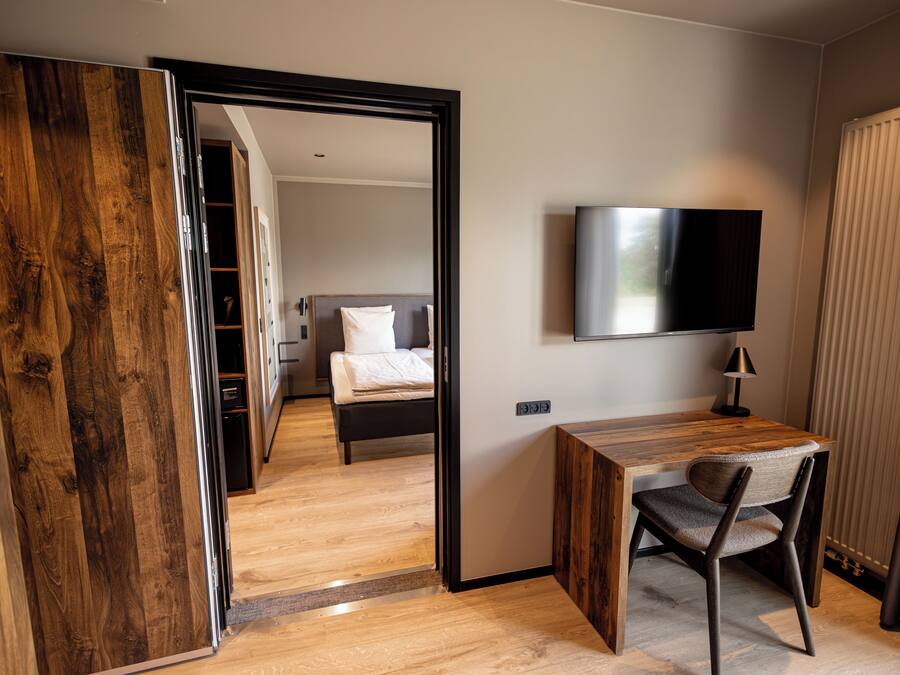 Ein Hotelzimmer mit Holzschreibtisch, einem Sessel, einem Bett, einem Fernseher und einem Kleiderschrank.