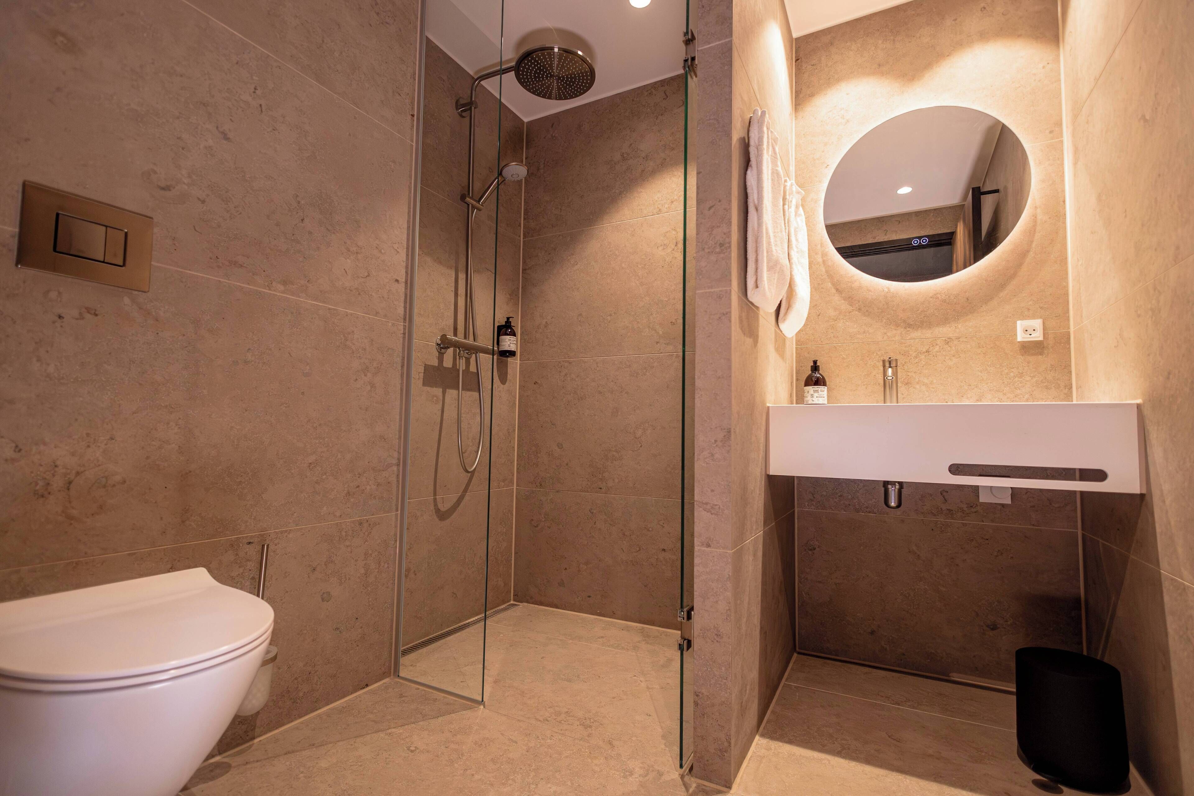 A modern bathroom with a glass-enclosed shower, a white toilet, a sink with a mirror, and a towel hanging on the wall.