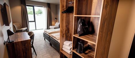 A hotel room with a wooden wardrobe, a desk, a bed, and a view of the outdoors.