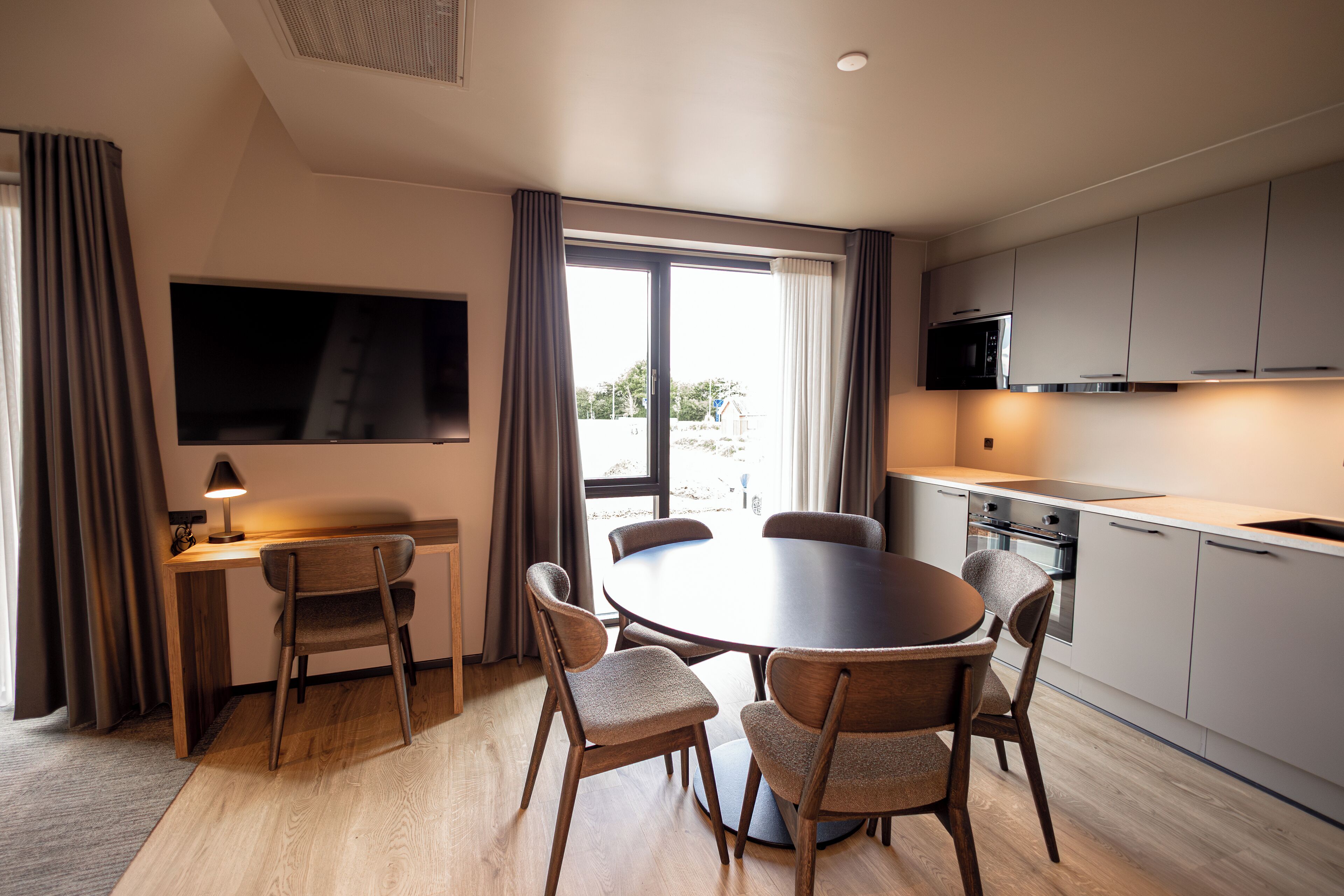A modern kitchen with a dining area, large windows, and a flat-screen TV.