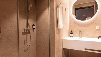 A modern bathroom with a glass-enclosed shower, a white sink, and a round mirror.