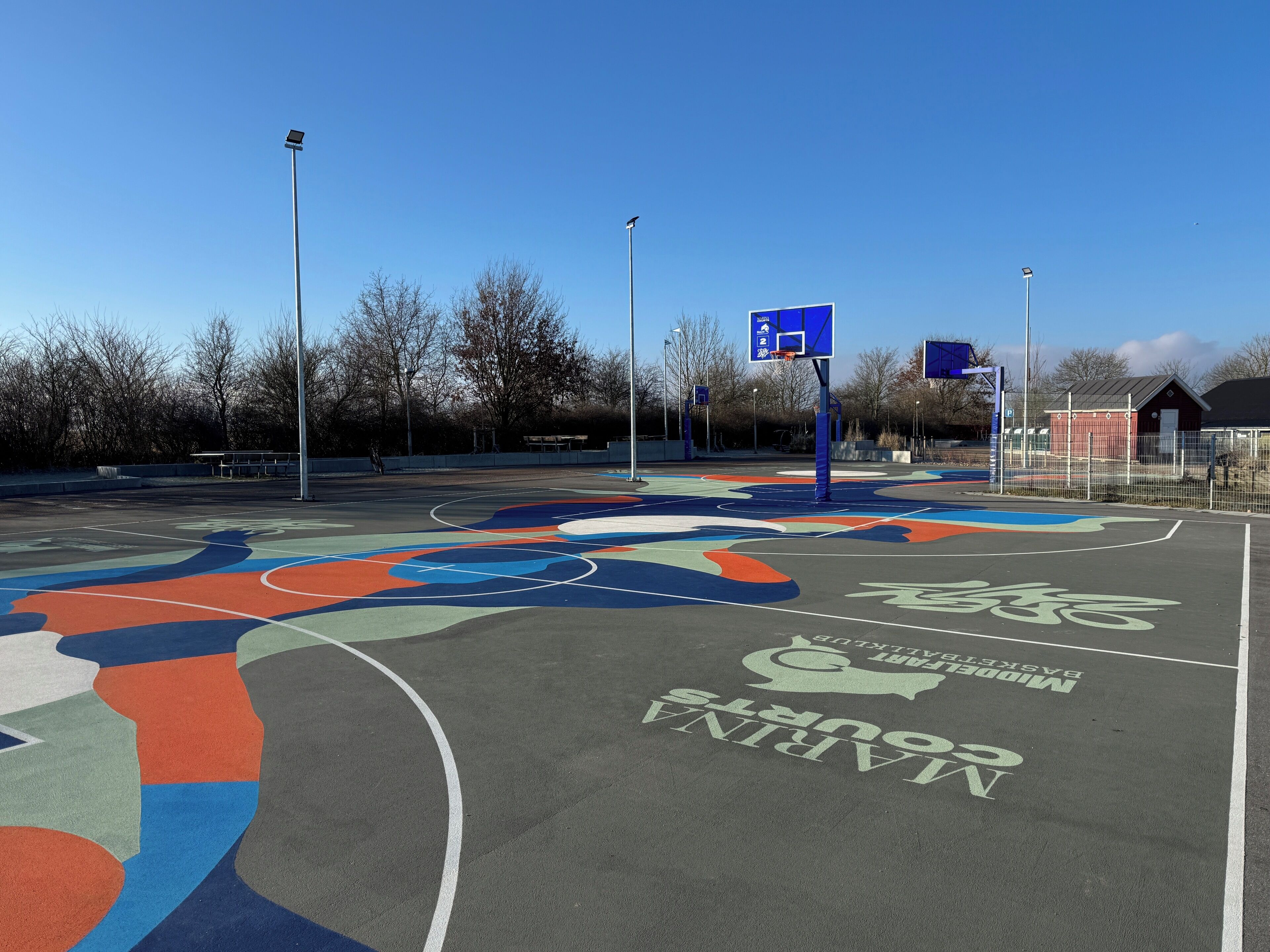 An outdoor basketball court with colorful markings and a blue basketball hoop.
