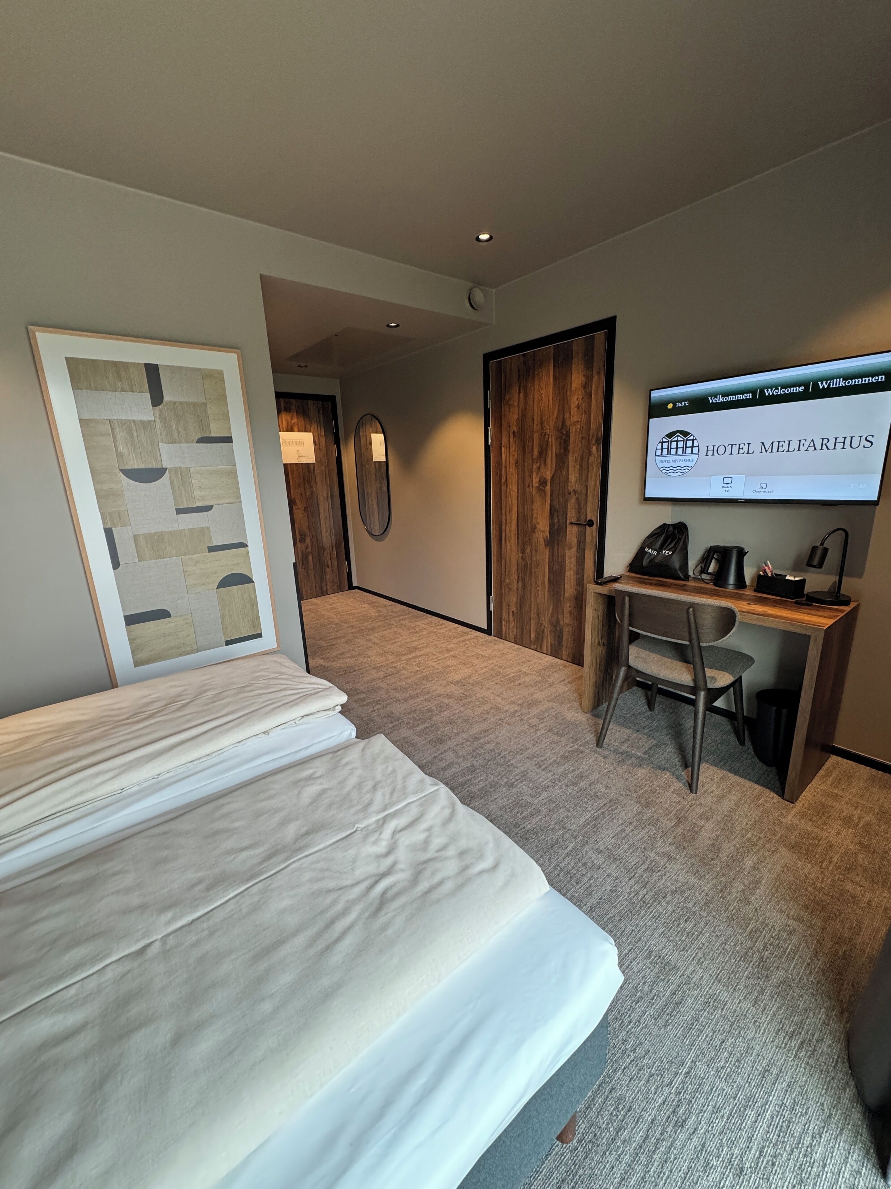 Een hotelkamer met een bed, een bureau en een televisie waarop 'HOTEL MELFAHRUS' staat.