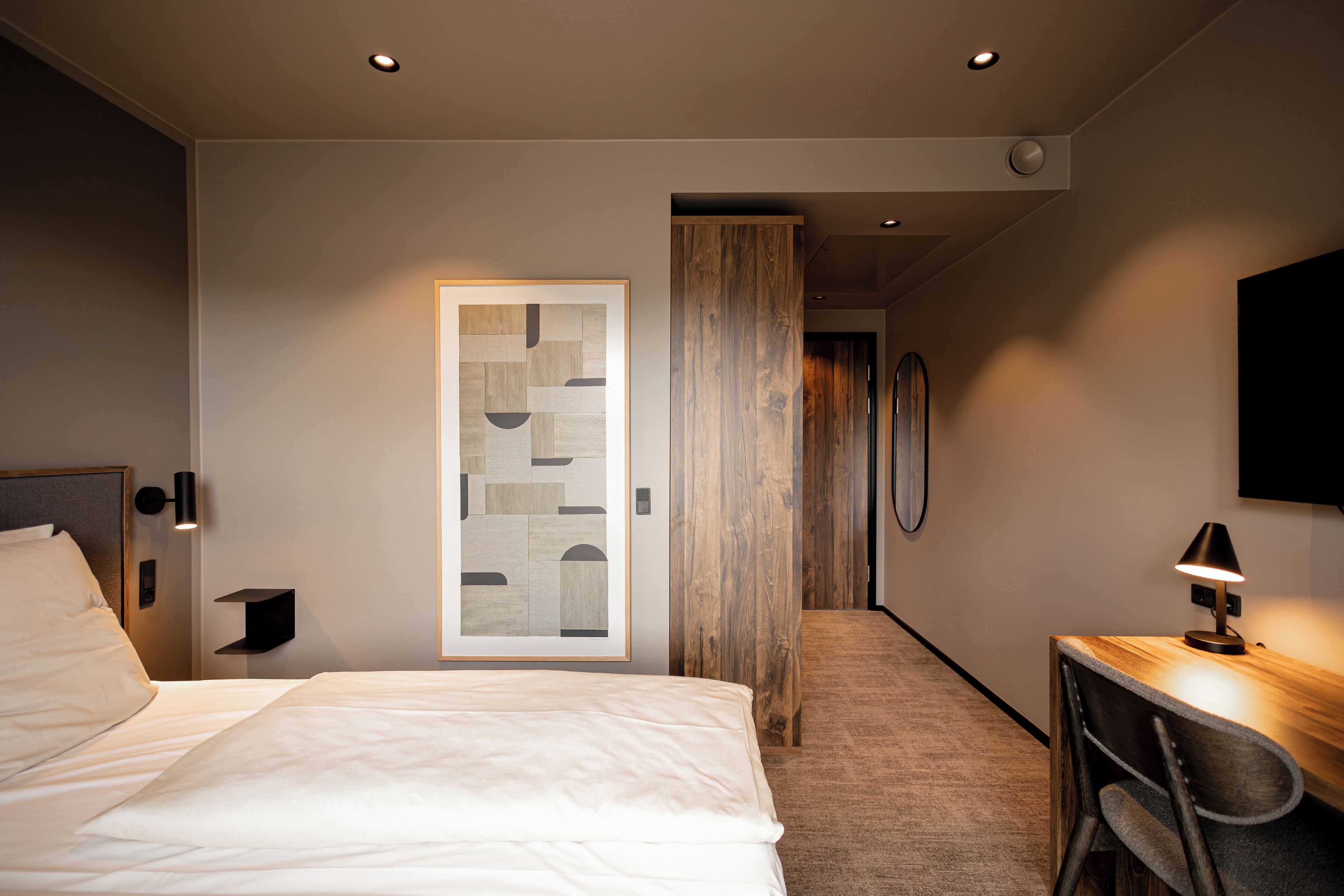 Une chambre d’hôtel comprenant un lit, un bureau avec une chaise, une armoire en bois et un téléviseur fixé au mur.