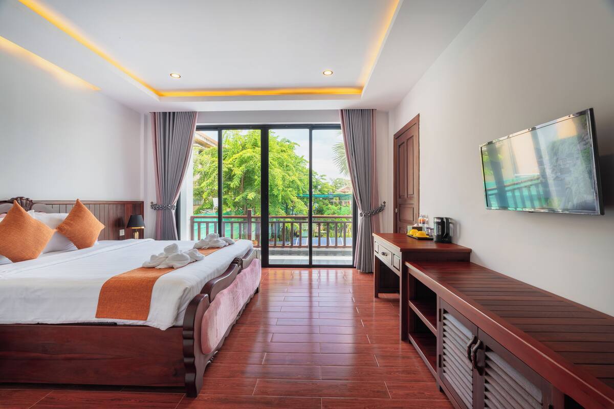 Een hotelkamer met een groot bed, een aan de muur bevestigde televisie, en een balkon met uitzicht op groen.