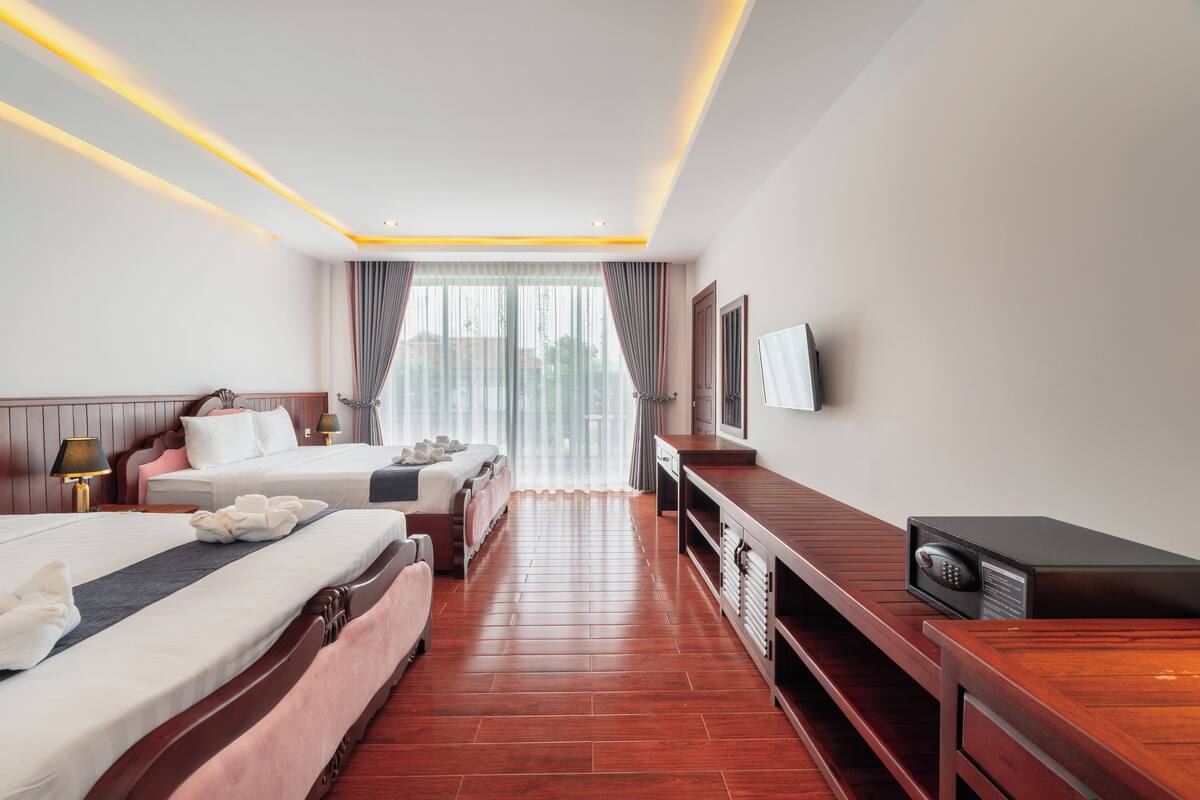 Een hotelkamer met twee bedden, een bureau, een televisie en een raam met gordijnen.