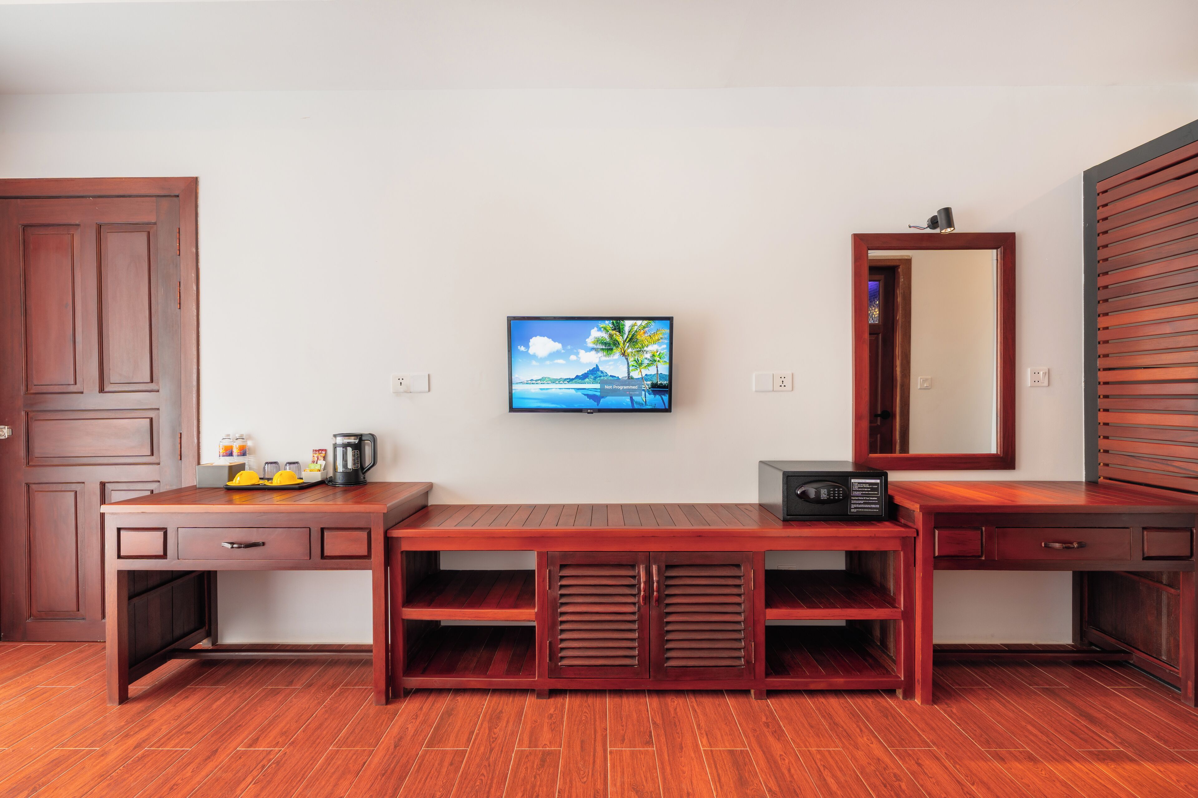 A wooden desk with a flat-screen TV, a coffee maker, and a radio.