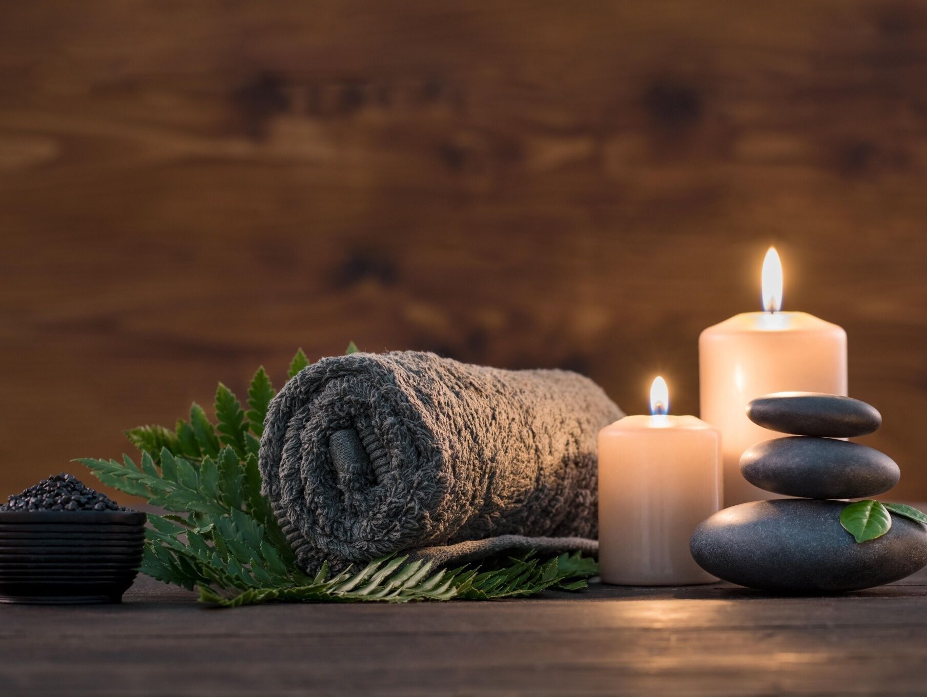A wooden background with a rolled towel, a lit candle, a stack of stones, and a bowl of black beans.