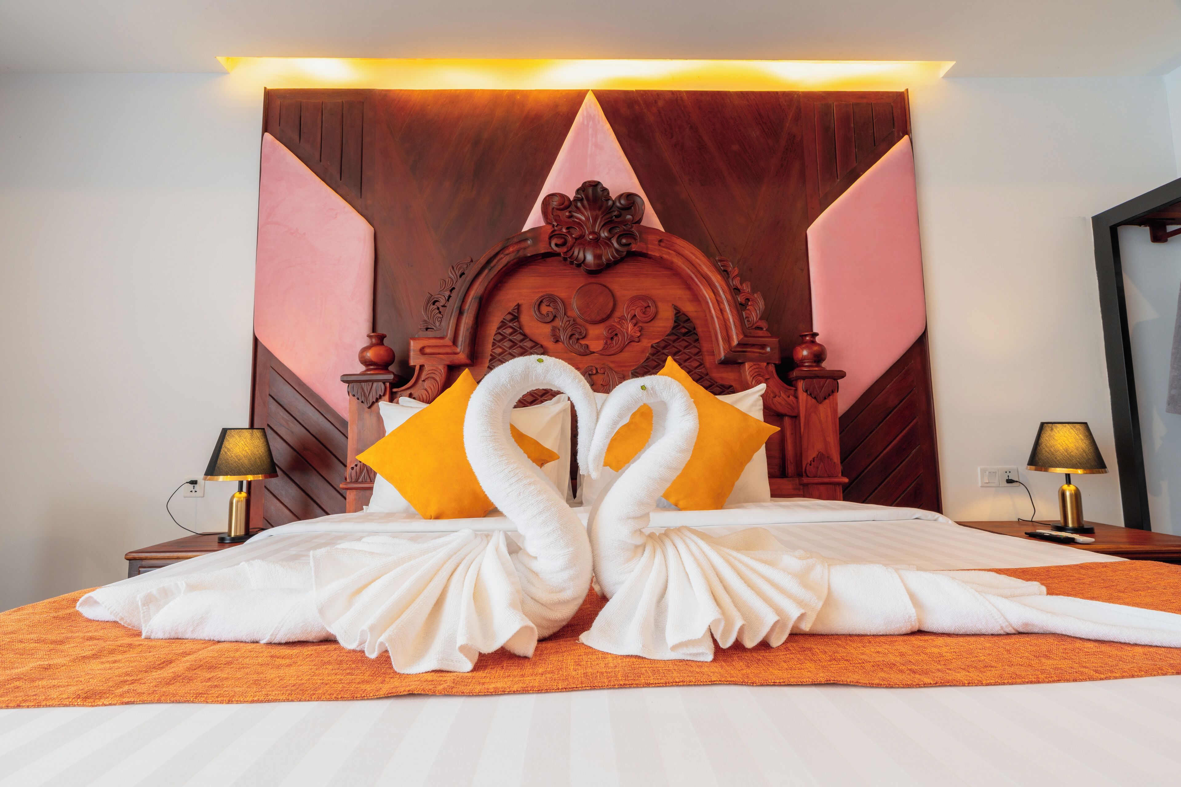 A hotel room with a large bed, a wooden headboard, two lamps, and a wall-mounted light fixture.