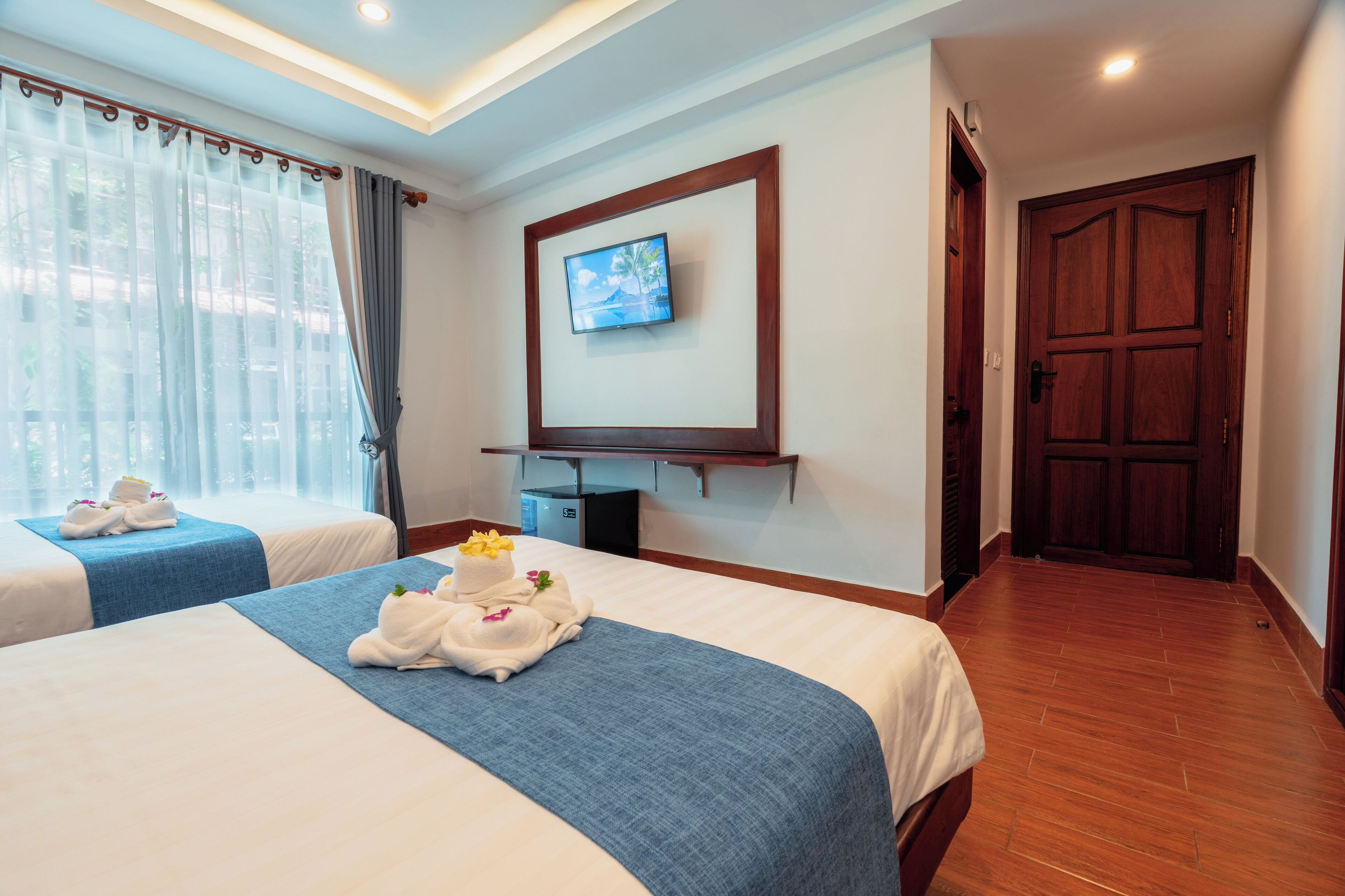Una habitación de hotel con dos camas, un televisor montado en la pared y una puerta de madera.