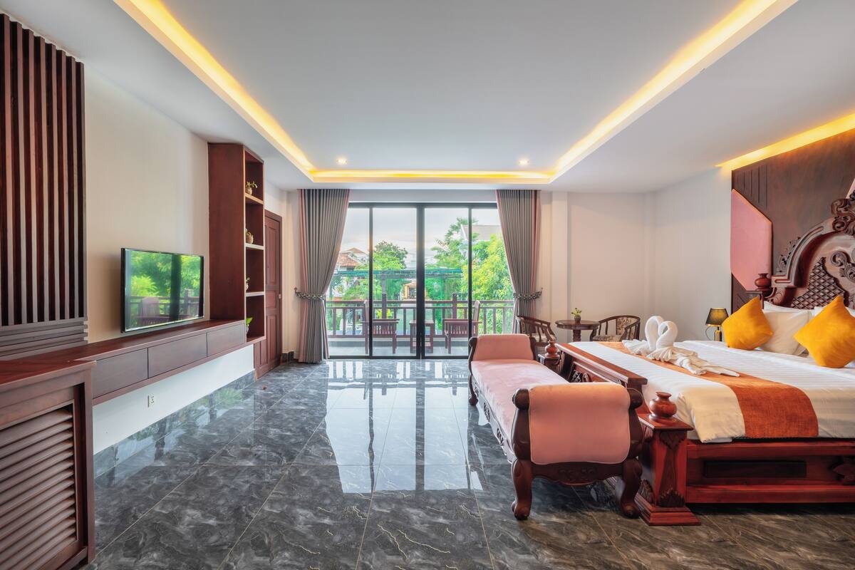 Een hotelkamer met een groot bed, een televisie, een balkon met uitzicht op groen en een houten kast.