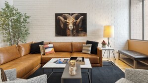 A modern living room with a brown leather sofa, a coffee table, a lamp, and a large ram picture on the wall.
