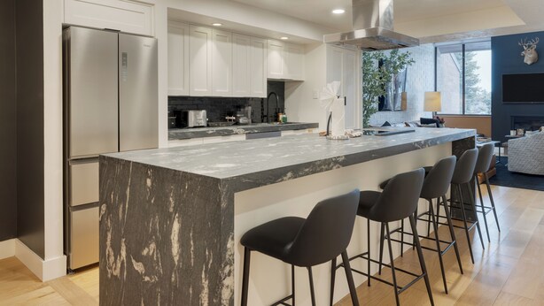 A modern kitchen with a large island, bar stools, and a built-in stove.