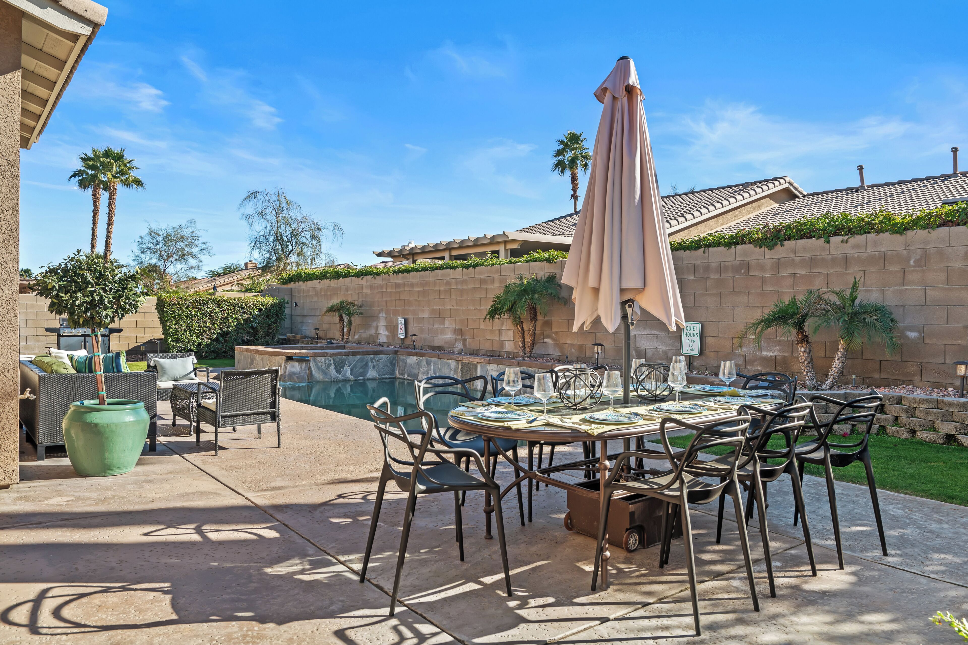 A patio area with a pool, outdoor furniture, and a table set for dining.