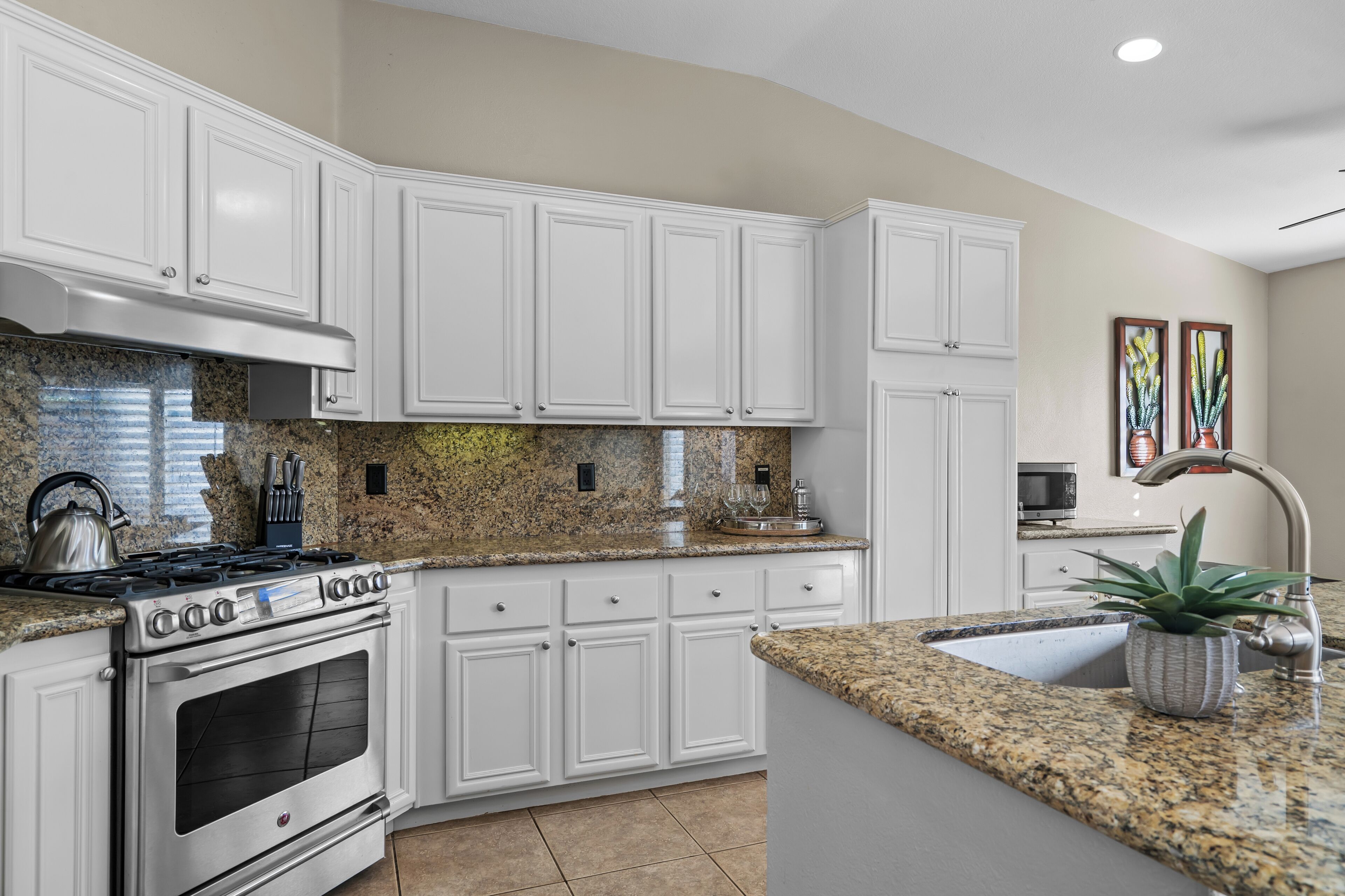 A kitchen with white cabinets, a granite countertop, a stainless steel stove, and a sink.