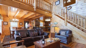 Ein Holzblockhaus-Interieur mit Treppe, Ledersofas, Essbereich und Küche.