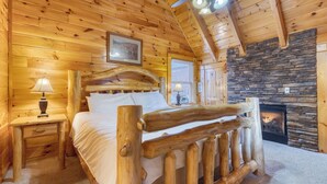 Ein Schlafzimmer in einer Blockhütte mit Kamin aus Stein, einem Bettgestell aus Holz und einem Deckenventilator.