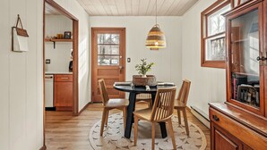 A dining area with a round table, wooden chairs, a woven basket centerpiece, and a hanging light fixture.