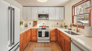 A modern kitchen with white cabinets, a stainless steel refrigerator, a built-in oven, and a microwave.