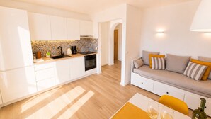 Eine moderne Küche mit weißen Schränken, einem eingebauten Backofen und einer Fliesenspiegel mit Muster. Es gibt einen Essbereich mit Tisch, Stühlen und einer Couch mit Kissen.