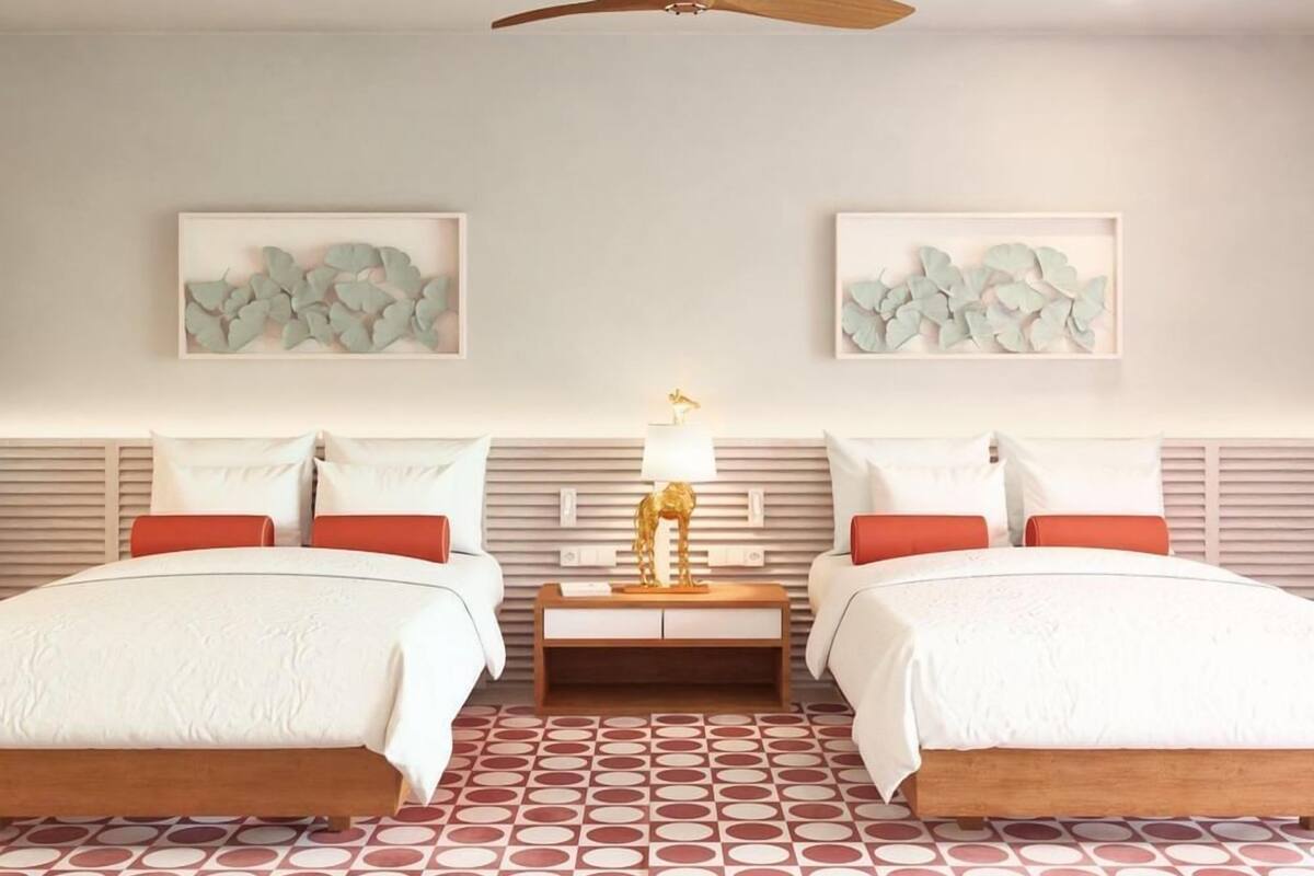 A hotel room with two beds, a nightstand with a lamp, and artwork on the walls.