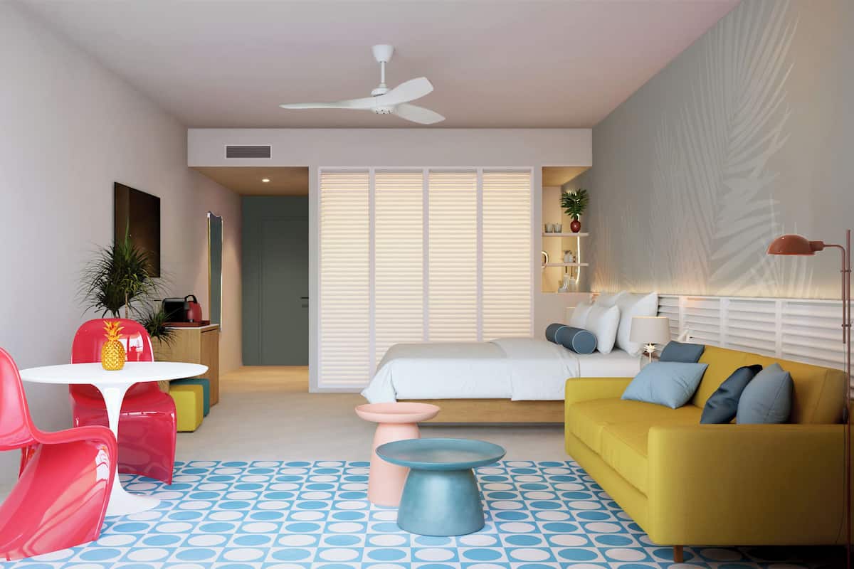 A modern, well-lit room with a yellow sofa, a red chair, a small table, and a bed with white bedding.