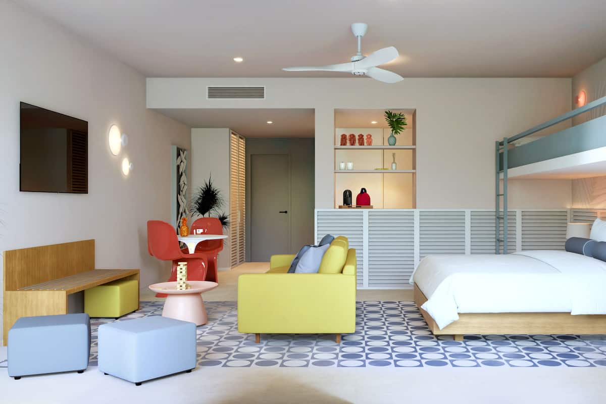 A modern, well-lit bedroom with a bunk bed, a desk with a chair, a sofa, and a small dining table.