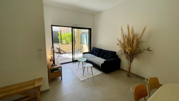 A modern living room with a black sofa, a small table, a bench, and a potted plant. - Eco-responsible haven of peace in Golfe-Juan: new serviced apartment (Vallauris)