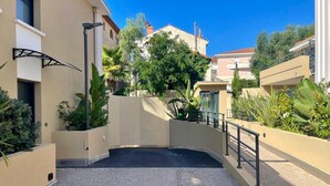 A modern building with a curved entrance, a small elevator, and a gated area with lush greenery. - Eco-responsible haven of peace in Golfe-Juan: new serviced apartment (Vallauris)