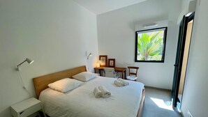 A modern bedroom with a large bed, bedside tables, a desk, and a window with a view of greenery. - Eco-responsible haven of peace in Golfe-Juan: new serviced apartment (Vallauris)
